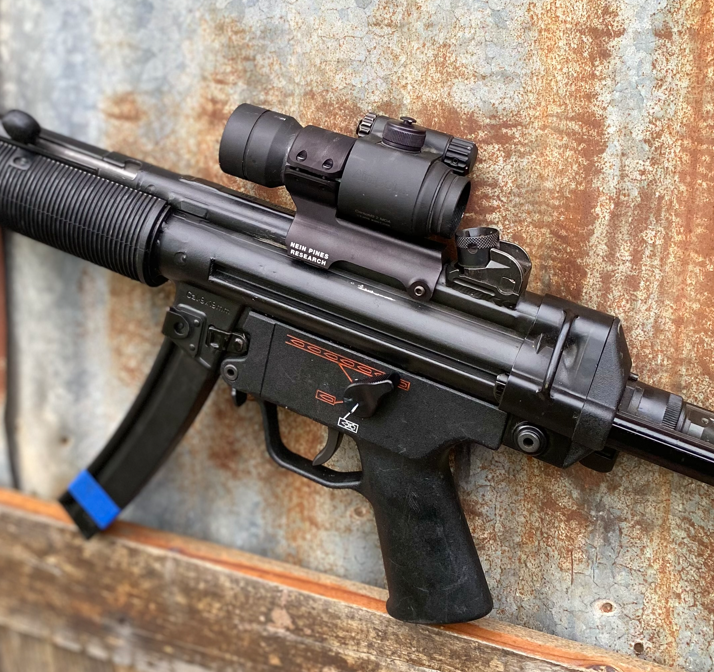 MP5 with the Nein Pines Gretel low mount and a 30mm red dot sight against a rusted metal wall