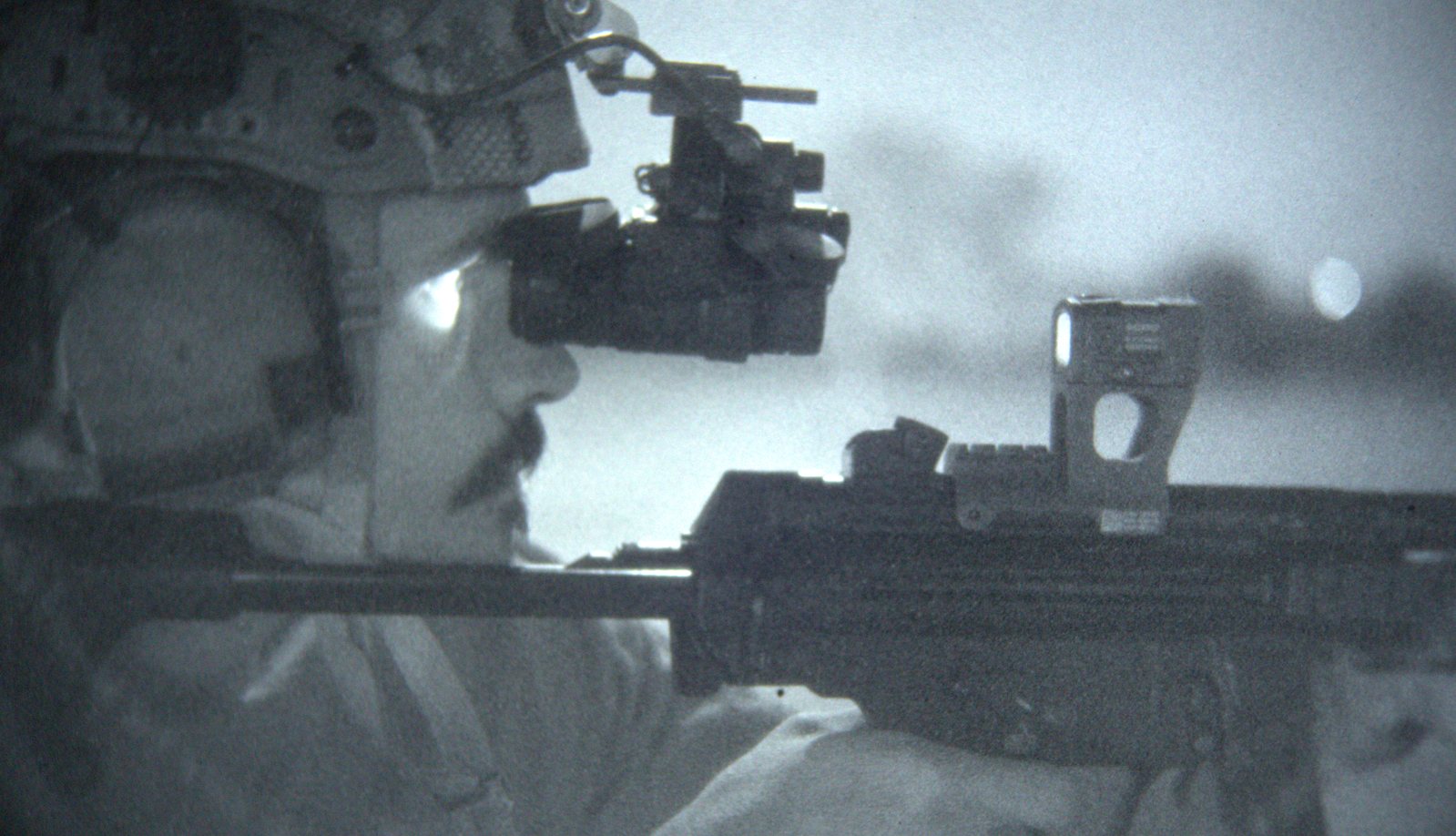 Shooter passively aiming an MP5 fitted with the Hansel optics mount and red dot through helmet-mounted night vision